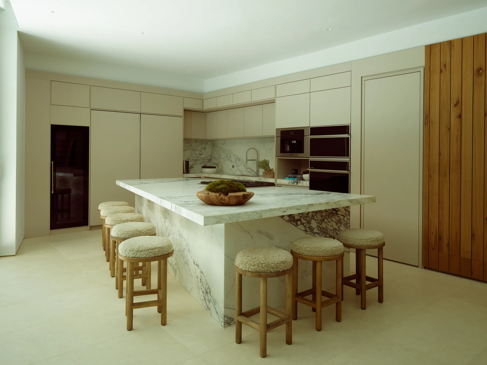 Renovated kitchen with an oak-and-stone island and bar seating in the Onaway residence by LUXOM, Miami