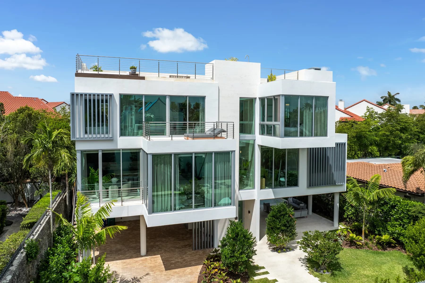Aerial exterior view of Luxom's completed Crystal Residence in Coconut Grove, Miami, showing its vertical stack of glass walled floors and rooftop garden above the surrounding rooflines