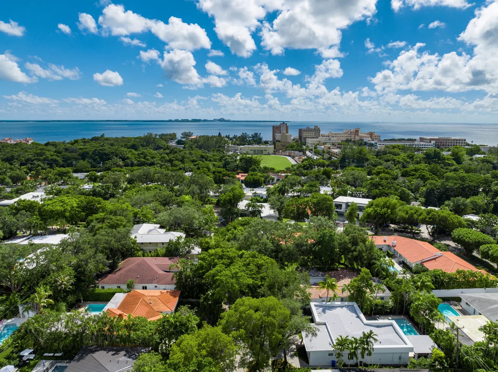 Aerial view of adjacent Coconut Grove lots and tree canopy stretching toward Biscayne Bay, showing how each parcel sits beside the next