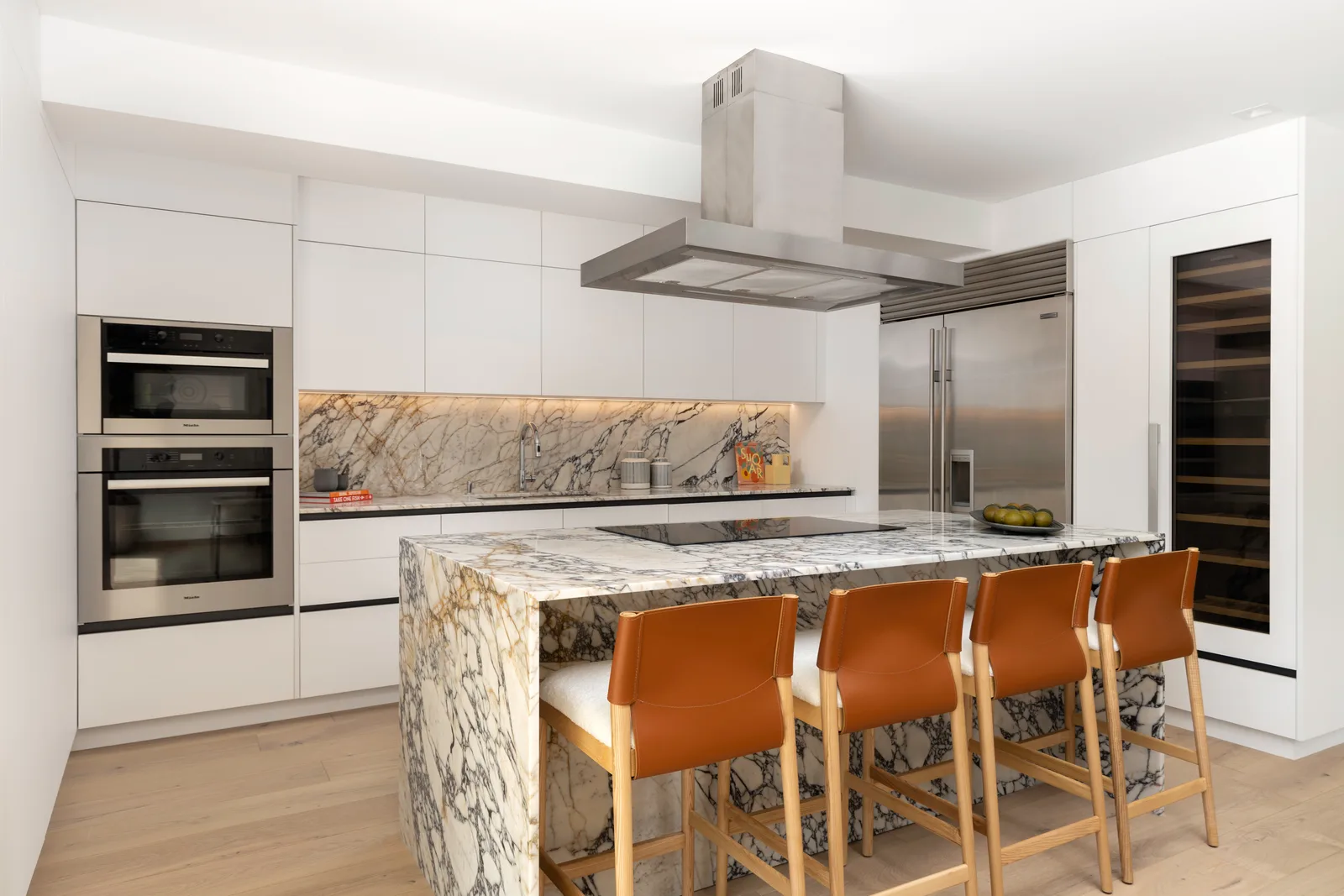 The finished kitchen at Luxom's Samana Residence in Coconut Grove, with a grey and gold marble waterfall island wrapping down to the floor against white cabinetry